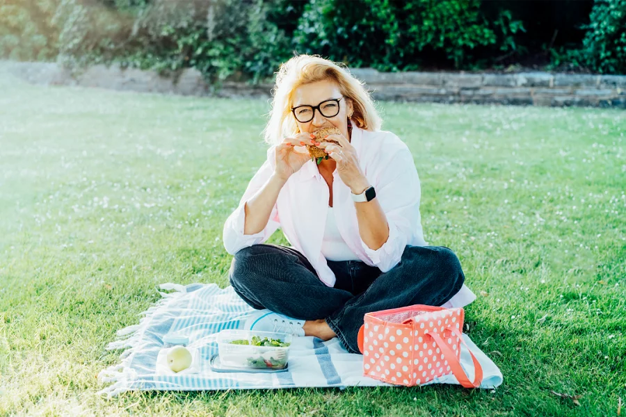 A woman sitting on grass and eating a healthy burger from her lunch box